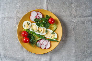 Fototapeta na wymiar salad with cucumber egg tomato onion parsley dill in a yellow plate on a gray linen tablecloth selective focus