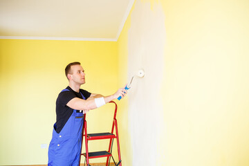 Young man in overalls hold a paint roller. Tools accessories for apartment room renovation. Home renovation concept