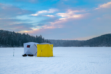 Ice fishing tent on a frozen lake at sunset. Fisherman camp on a peaceful winter evening.