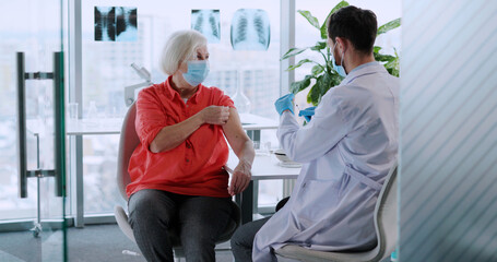 Elderly Female Patient Visiting Doctor in hospital for Vaccination. Caucasian Pharmacist Injecting Coronavirus Vaccine into Woman s Arm. Healthcare.