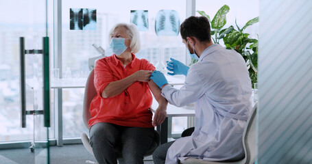 Young caucasian doctor injecting senior woman patient and prescribing medicine in laboratory...