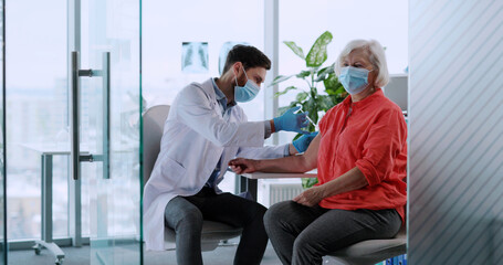 Vaccination concept. Eoderly blonde woman visiting doctor therapist taking injection vaccine against coronavirus influenza. Patient.