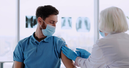 Obraz premium Young caucasian man participating in vaccination in medical laboratory. Doctor injecting experimental coronavirus vaccine for male customer patient.