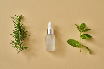 Essential oil bottle with fresh peppermint and rosemary leaves on pastel yellow background