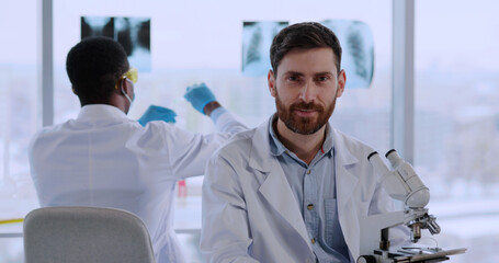 Portrait of caucasian bearded professional lab scientist removing face mask smiling to camera. Medical people. Hospital environment.