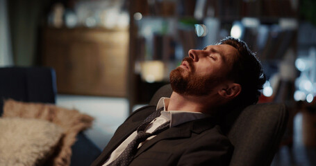 Tired young businessman returning home removing suit tie relaxing on the sofa. Living room apartment. Corporate person ;lifestyle. Workaholic.