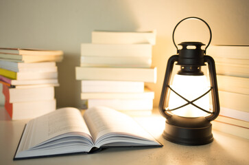 Fototapeta na wymiar Kerosene lamp lit on a table with stacked books and an open book. Knowledge concept.