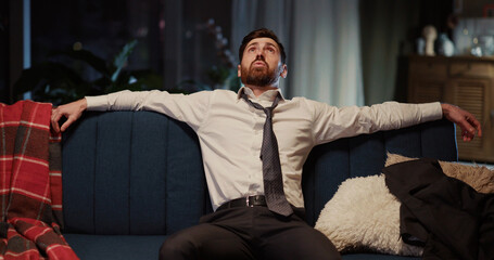 Handsome young male executive returning home sitting on cozy couch in living room resting down enjoying evening. Businessman. Business lifestyle.