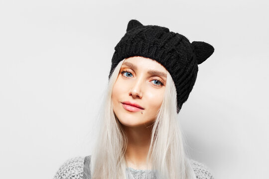 Studio portrait of young blonde pretty girl wearing black hat with cat ears on white background.