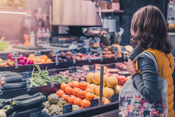 woman in yellow vest and mask buying Mediterranean fruits and vegetables in a traditional market. healthy food and Mediterranean diet of proximity.