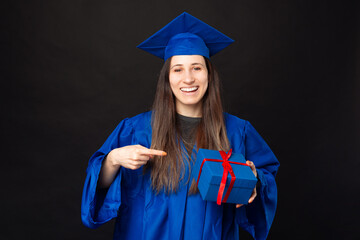 Happy young student woman pointing at gift box and wearing blue bachelor