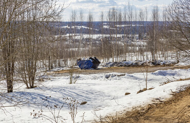 A huge blue iron container with garbage stands in a winter field among the trees