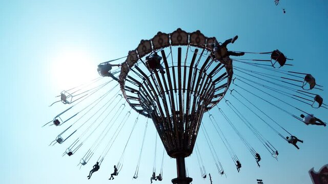 Silhouettes having fun riding on a chain carousel in the amusement park