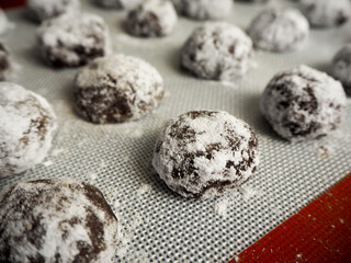 close to the raw chocolate marble cookies in powdered sugar before baking lies on a silicone white mat. side view . cooking sweets
