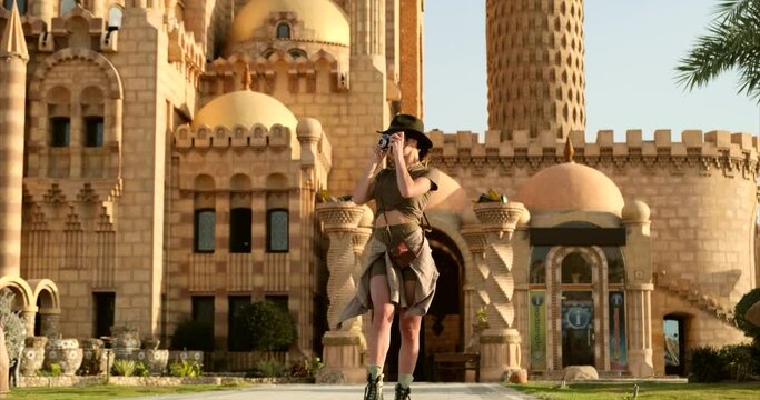 a slender girl, a tourist, travels alone in the eastern countries of the Persian Gulf, in short tourist shorts, a shirt and a discovery-style felt hat, takes a photo of the old temple
