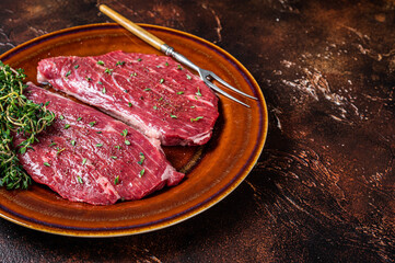 Raw rump cap steak or top sirloin steak in rustic plate with thyme and olive oil. Dark background. Top view. Copy space