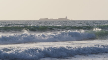 Fototapeta na wymiar Vista desde la Playa de la Barrosa del Castillo de Sancti Petri en Cádiz con olas rompiendo. Castillo en el mar.