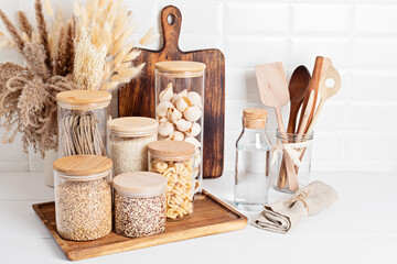 Assortment of grains, cereals and pasta in glass jars and kitchen utensils on wooden table. Healthy balanced food, sustainable lifestyle, zero waste storage, eco friendly idea - Powered by Adobe