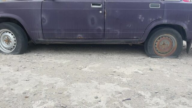 Close up of old car with deflated wheels. Abandoned car with damaged wheels parked on city street.