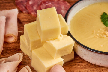cubos de queso partidos en cuadros con jamon y crema sobre una base de madera