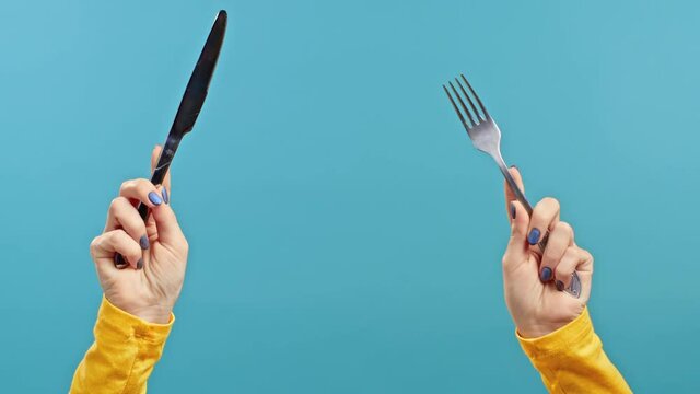 Hands of woman with fork and knife. Lady waiting for serving dinner dishes with cutlery on blue studio background. Only hands.