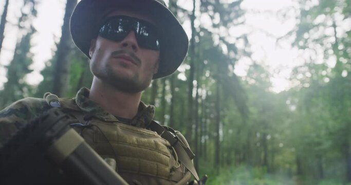 Modern soldier with rifle in dens forest with smoke in backgorund