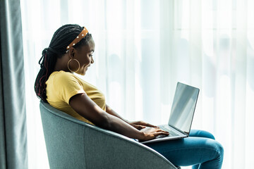 Young african american woman at home in the chair relaxing in her lliving room reading laptop surf...