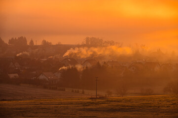 Air pollution, smoke from chimneys in the village, burning with solid fuel, ecological clouds, orange colors of morning light