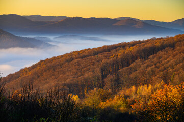 Autumn scenery, fog in the valley, orange sun over the mountains