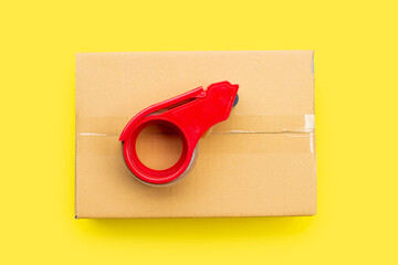 Packaging tape dispenser on cardboard box on yellow.