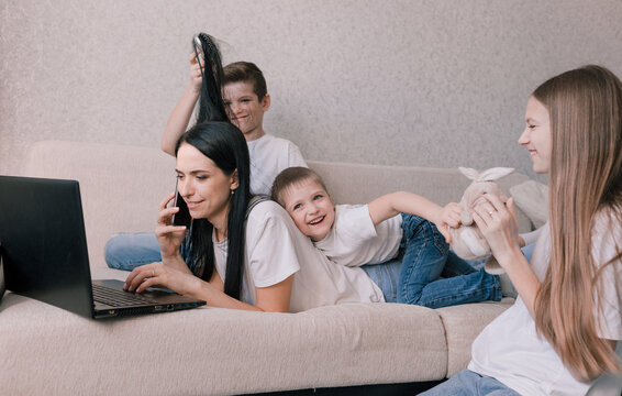 Active Children Indulge, Interfere And Distract Their Mother While Working At Home On A Laptop. Working During A Pandemic. Freelancer Remote Work