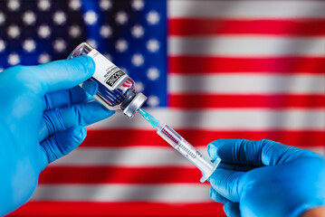Preparation of a dose of vaccine in a syringe with a vial of the antibiotic and in the background the flag of the EEUU. Doctor preparing vaccine injection for the vaccination campaign against disease