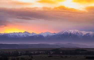 Obraz premium Dramatic early sunrise landscape over carpathian mountains range covered in snow with beautiful orange sky and clouds