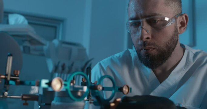 A male medical worker wearing black latex gloves and disposable eyeglasses is checking a detail on the axiosplit device and inside of it is the human ceramic model of a jaw.