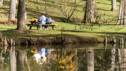 Young couple sitting at a wooden table having a picnic, by the lake, in early spring