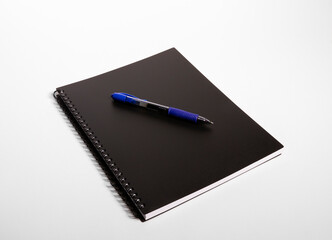 Blue pen on top of a black notebook against a white background