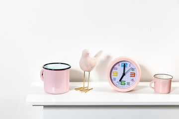 an alarm clock showing seven o'clock, cup, a pink bird figurine, a books on the table.