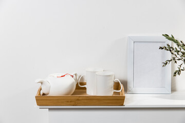Dry branch of eucalyptus in a white figured earthenware vase. A teapot two tall cups for tea in the wooden tray on the table. Scandinavian style. Copy space