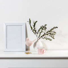 Dry branch of eucalyptus in a white figured earthenware vase. A figurine of a pink bird and a cup on the table. Scandinavian style