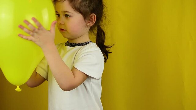 A yellow ball in the hands of a little girl. The child draws emoticons. Children's emotions. Positive emotions. Child with a balloon on a yellow background. Happy child with a balloon. 