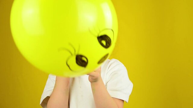 The baby is crying. Children's tantrums. Child with a balloon emoticon. Positive and negative emotions of the child. Hide emotions. Children's concept. Child with inflatable ball on yellow background