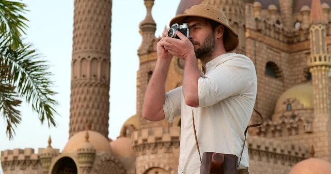 handsome man traveler in a retro hat and shirt with rolled up sleeves, takes a photo on a vintage film camera, near a medieval mosque, studies the archaeological heritage of Muslim culture.