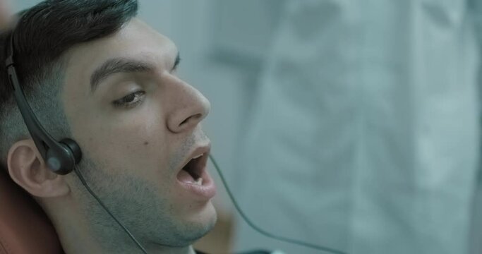 Close-up face of an Arabian male patient with an open mouth who is having a Joint vibration analysis procedure (JVA) and sitting in the dental chair at the dental clinic.