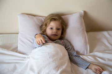Little girl lying in bed and playing, but can not sleep, on a white background