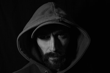 face of a man in shadows with cap and hood on a black background
