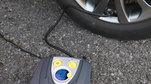 Electric tire inflator connected to car electrical system pumping up car tyre on the roadside.