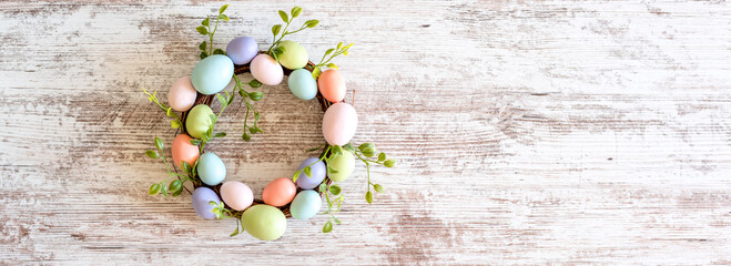 Rustic Easter banner with pastel colored egg wreath on white wood background