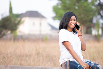 attractive young black woman sitting alone outdoor making a phone call, feeling happy and smiling