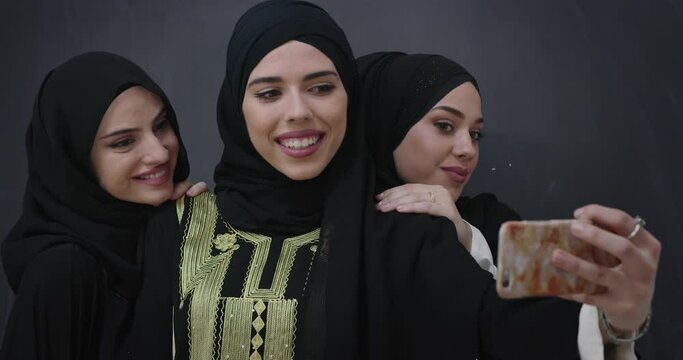 Group of young beautiful muslim women in fashionable dress with hijab using mobile phone taking selfie