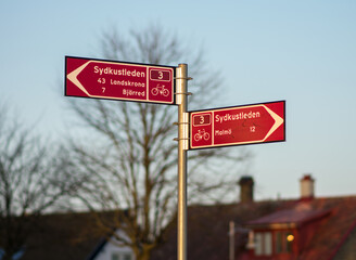 Street sign in central Lomma, marking cycling pathways on Sydkustleden, a trail along the swedish southern coast. Red signs in a street corner